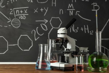 Modern mikroskop ve mataralar ahşap masada, kimyasal formüllerle birlikte.