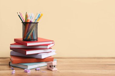 Renk duvarına karşı ahşap masa üzerinde kitap yığını ve farklı kırtasiye malzemesi