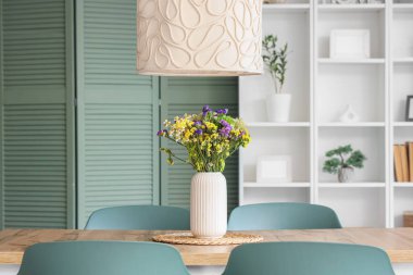 Yemek masasının üstünde kır çiçekleri olan vazo.