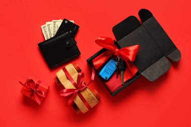 Yeni arabanın anahtarlarıyla hediye kutusu, kırmızı arka planda ahşap oyuncak ve cüzdan.