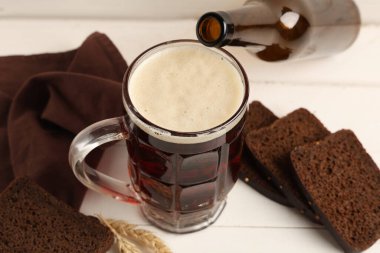 Beyaz ahşap arka planda ekmek dilimleri ve buğdaylı bir kupa taze kvass.