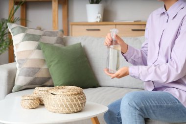Aroma spreyi şişesi olan kadın evdeki kanepede oturuyor, yakın plan.