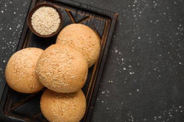 Tahta tahtada siyah zemin üzerinde susam tohumları olan taze çörekler.