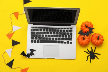 Sarı arka planda Cadılar Bayramı için modern dizüstü bilgisayar ve dekor kompozisyonu