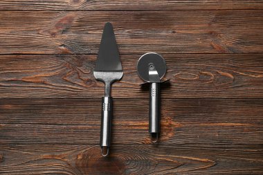 Paslanmaz çelik pizza kesicisi ve ahşap arka planda spatula.