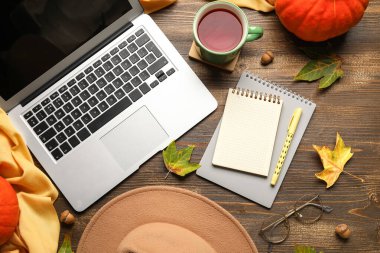 Not defterleri, çay fincanı ve ahşap arka planda sonbahar dekoru olan dizüstü bilgisayar.