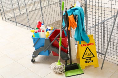 Temizlik malzemeleri, yer paspası ve ofisteki merdivenlere uyarı levhası konmuş kapıcı vagonu.