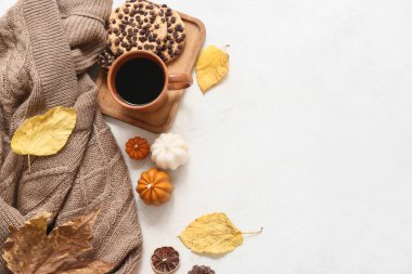 Kalın süveterli kompozisyon, bir fincan kahve, kurabiye ve arka planda sonbahar dekoru.