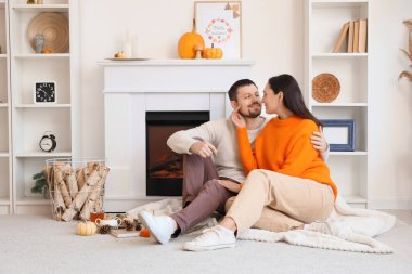 Sonbahar dekoru olan mutlu genç çift şöminenin yanında oturuyor.