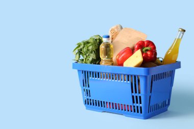 Farklı taze ürünlerle dolu mavi alışveriş sepeti ve mavi arka planda bir şişe yağ.