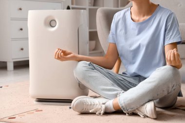 Hava nemlendiricisi olan genç bir kadın evde yerde meditasyon yapıyor.