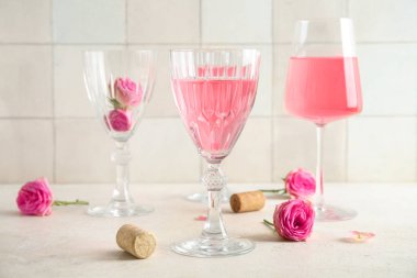 Beyaz fayans zeminine karşı masasında güller ve mantarlarla pembe şarap kadehleri