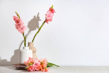 Güzel gladiolus çiçekli vazolar ve beyaz arka planda duran kitaplar.