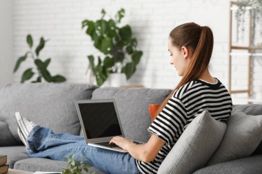 Evdeki kanepede oturan dizüstü bilgisayarı ve çay bardağıyla güzel bir kadın yazar.