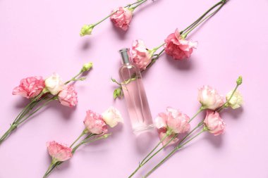 Bir şişe parfüm ve pembe arka planda Eustoma çiçekleri.