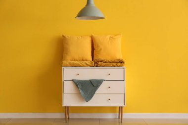 Sarı duvarın yanındaki klozette katlanmış battaniyeli yastıklar.