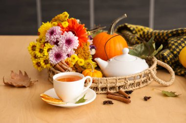 Hasır tabla, çaydanlık, bir fincan sıcak yeşil çay, çiçekler ve sonbahar yaprakları mutfakta.