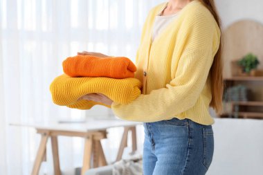 Evde bir yığın temiz giysi tutan genç bir kadın.