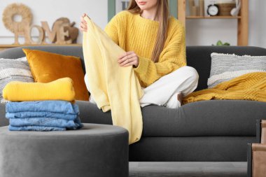 Evdeki kanepede temiz giysileri katlayan genç bir kadın.