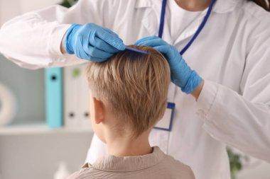 Klinikte küçük çocuğun saçını pedikülozla tarayan kadın doktor, yakın plan.