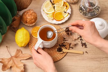 Kekin yanında bir fincan yeşil çay, masada limonlu tabak ve sonbahar dekoru olan kadın elleri. Yakın çekim.