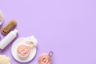 Doğal vücut fırçası, bir şişe kozmetik ürün ve leylak arkaplan üzerine banyo malzemeleri.