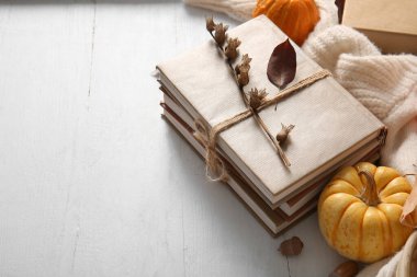 Kitap yığını, balkabağı ve kalın giysiler hafif ahşap arka planda