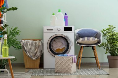 Çamaşır makinesi, sepet ve sandalyeli çamaşır odasının içi.