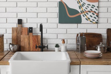 Mutfaktaki beyaz tuğla duvarın yanında lavabo ve çatal bıçaklarla dolu bir masa.