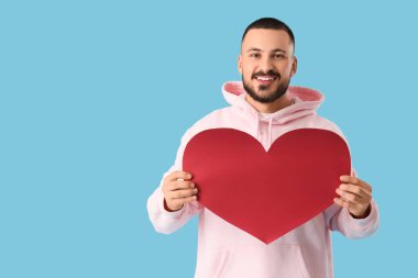 Mavi arka planda kağıt kalpli yakışıklı bir genç.