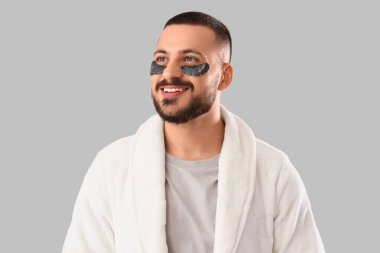 Gri arka planda göz bantları olan bornozlu genç bir adam.