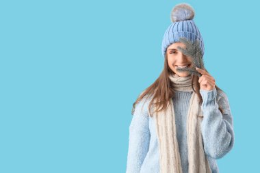 Güzel, genç bir kadın, şık ve sıcak kıyafetler içinde. Mavi arka planda Noel ağacı dalı var.