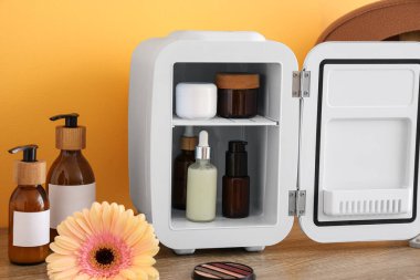 Küçük buzdolabı, kozmetik ürünleri ve sarı duvarın yanındaki çiçekli masa. Yakın çekim.