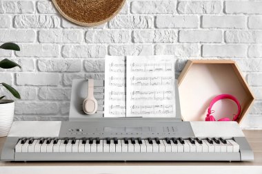Beyaz tuğla duvarın yanında nota kağıtları ve kulaklıkları olan modern sentezleyici