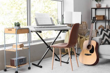 Koltuklu, sentezleyicili ve gitarlı bir oturma odası.