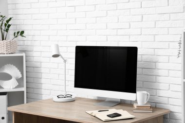 Beyaz tuğla duvarın yanında bilgisayarı olan modern ofis.