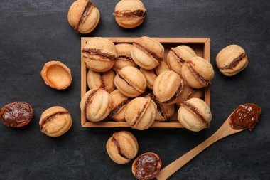 Ahşap kutu, tatlı ceviz şeklinde kurabiyeler ve siyah arka planda kaynamış konsantre süt.