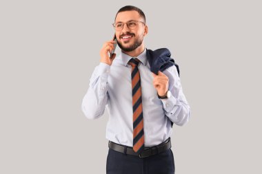 Kravatlı genç işadamı arka planda cep telefonuyla konuşuyor.