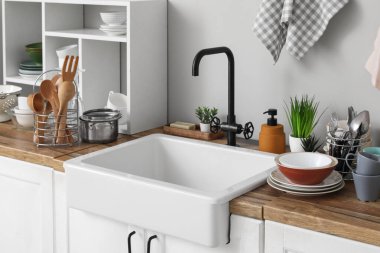 Seramik lavabo, temiz bulaşıklar ve ahşap mutfak tezgahındaki raf ünitesi.