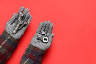 Kırmızı arka planda cıvata ve fındık tutan tamircinin elleri