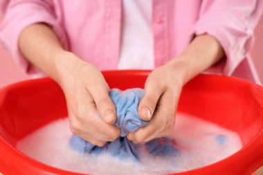 Çamaşırları leğende köpükle yıkayan kadın ve pembe arka planda su, yakın plan.