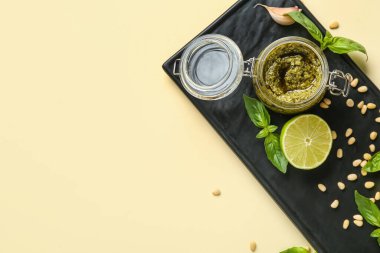 İçinde bir kavanoz lezzetli pesto sosu ve bej arka planda malzemeler olan pano.