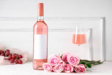 Beyaz arka planda güzel güller olan bir şişe ve bir bardak pembe şarap.