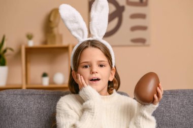 Oturma odasında çikolata yumurtası olan tavşan kulaklı küçük bir kız.