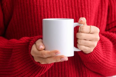 Sıcak kırmızı kazaklı bir kadın beyaz arka planda seramik bardak tutuyor. Yakın çekim.