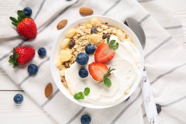 Beyaz ahşap arka planda sağlıklı mısır gevreği, yoğurt ve böğürtlen kâsesi.