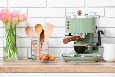 Modern kahve makinesi, bir bardak sıcak espresso ve bir tabak tatlı kekler mutfakta beyaz tuğla duvarın yanında.