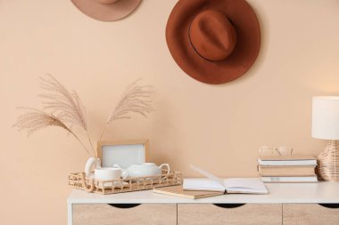 İş yerinde çaydanlıklı kitaplar, odada bej duvarın yanında bir fincan çay ve dekor. Yakın çekim.