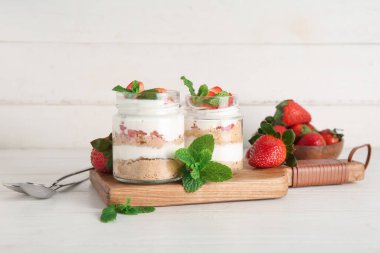 Beyaz ahşap arka planda lezzetli çilekli cheesecake ile kavanozlar.