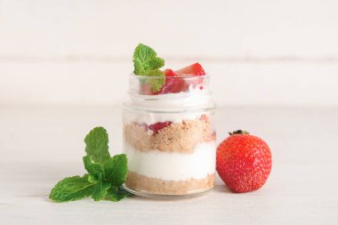 Beyaz ahşap arka planda lezzetli çilekli cheesecake ile kavanoz